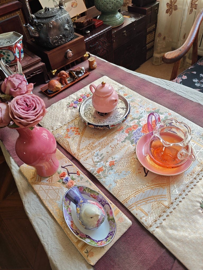 Gold floral Nishijin tea mat with a pink teapot and glass pitcher.